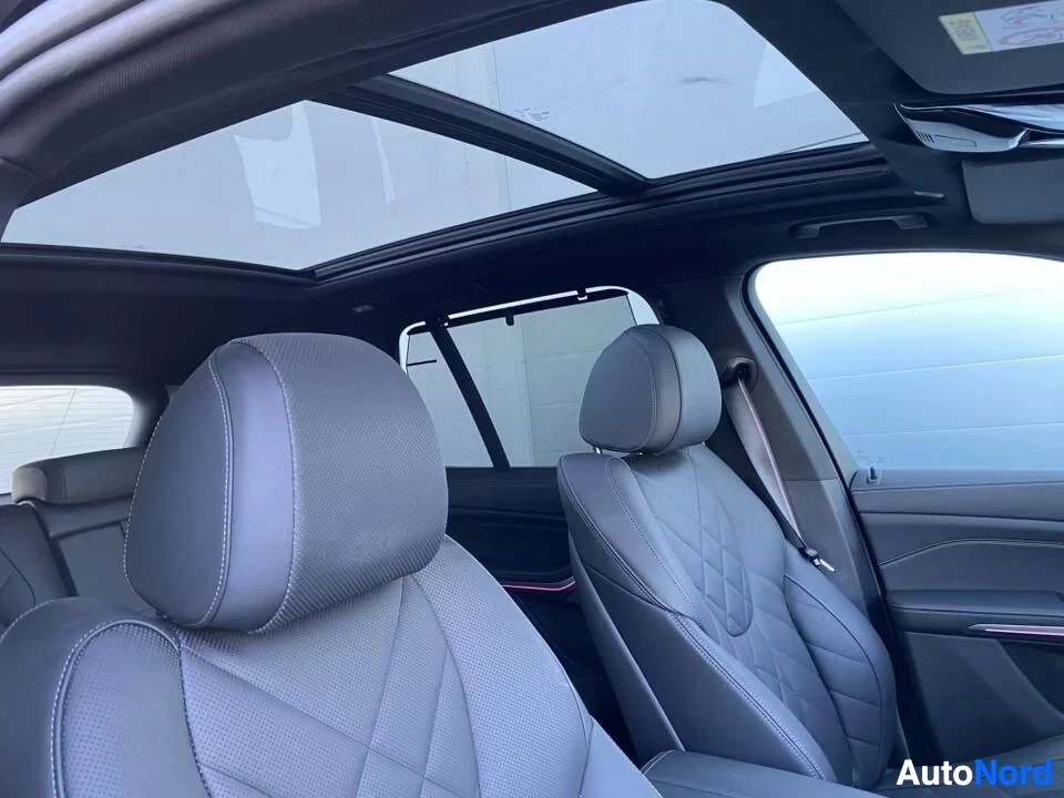 Ohjaamo: Auton sisäänotto sivulta taaksepäin. Näkyy panoraamakatosta, etumatkustajan istuimen selkänoja ja kuljettajan istuimen headrest. Istuimet ovat vaalealla verhoil