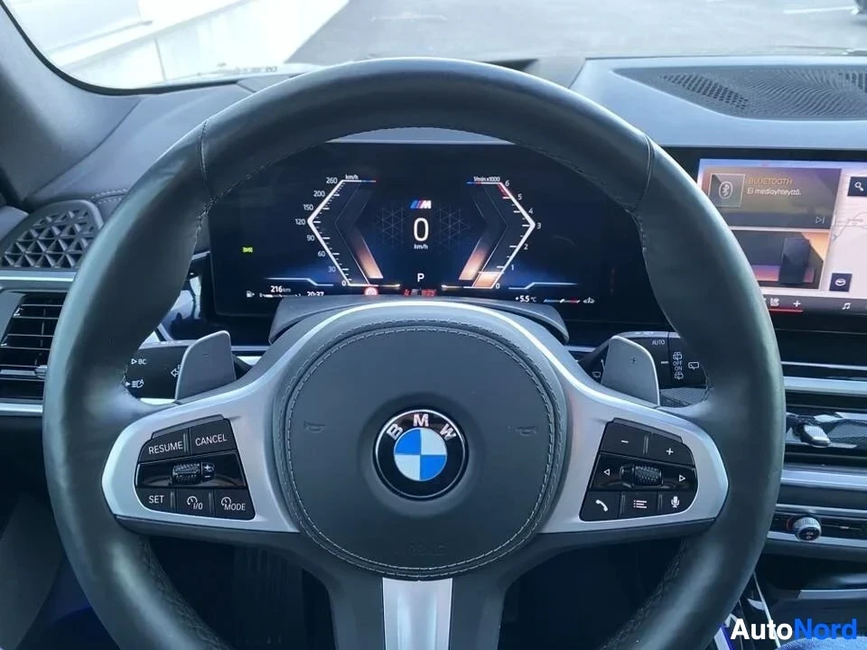 Ohjaamo: BMW-ohjauspyörä M-logolla, digitaalinen mittaristo näyttää 0 km/h, multifunction-painikkeet ja cruise control -painikkeet näkyvissä, infotainment-näyttö oikeall