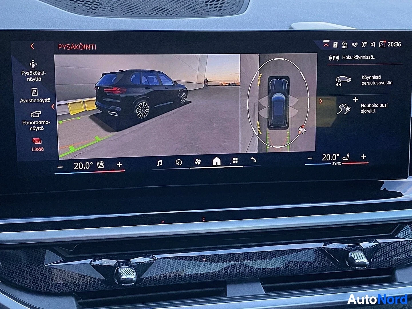 Yksityiskohta: Ajoneuvon panoraamakamera-näyttö näyttää 360-asteen kuvaa mustasta SUV-autosta sivusta ja ylhäältä parkkipaikalla. Näytössä näkyvät kellonaikaa 20:36 ja keltais