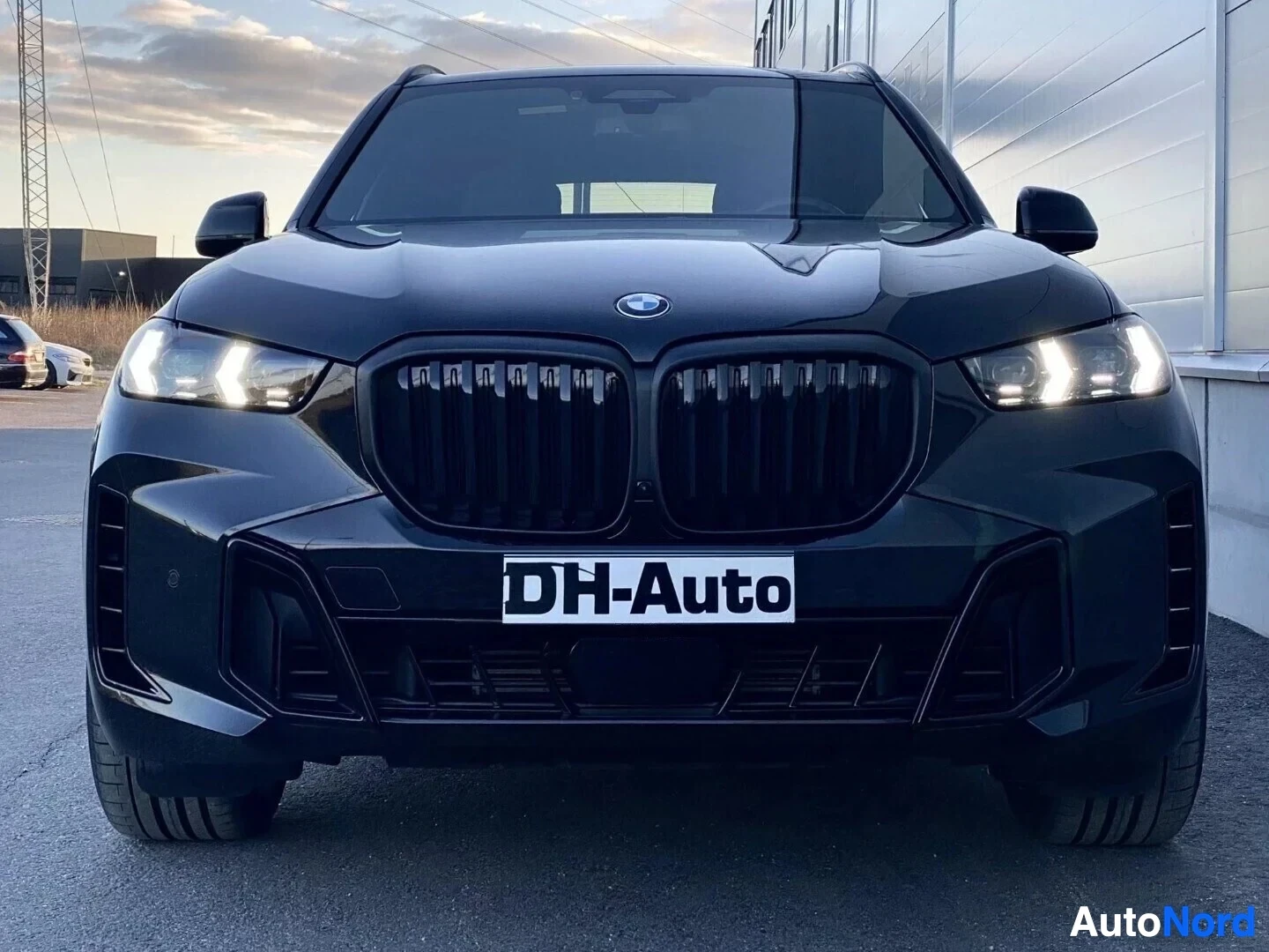 Edestä: Musta BMW X5 -maasturi etupuolesta kuvattuna. Näkyvissä kaksoiskuparit LED-ajovalot, musta säleikkö, DH-Auto-kilpi rekisterikilvessä ja mustat terän muotoiset s
