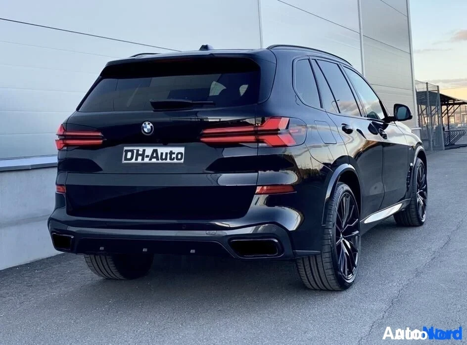 Takaviisto: Musta BMW X5 -henkilöauto takaa oikealta kuvattuna, takavalot päällä. Takaluukun päällä on DH-Auto-kilpi ja alhaalla kaksi pakoputken ulostuloa.