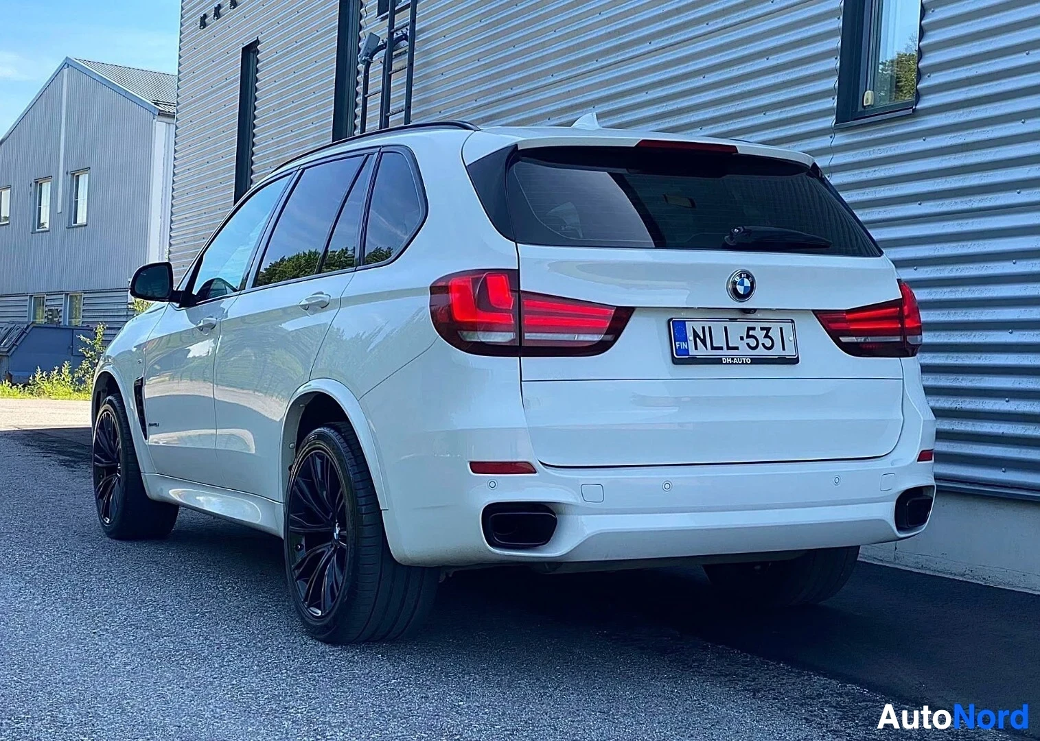 Takaviisto: Valkoinen BMW X5 -maasturi sivusta kuvattuna, oikealle katsottavissa, tummat pyörät, punaisen ja valkean väriset takavalaisimet, rekisterikilvessä