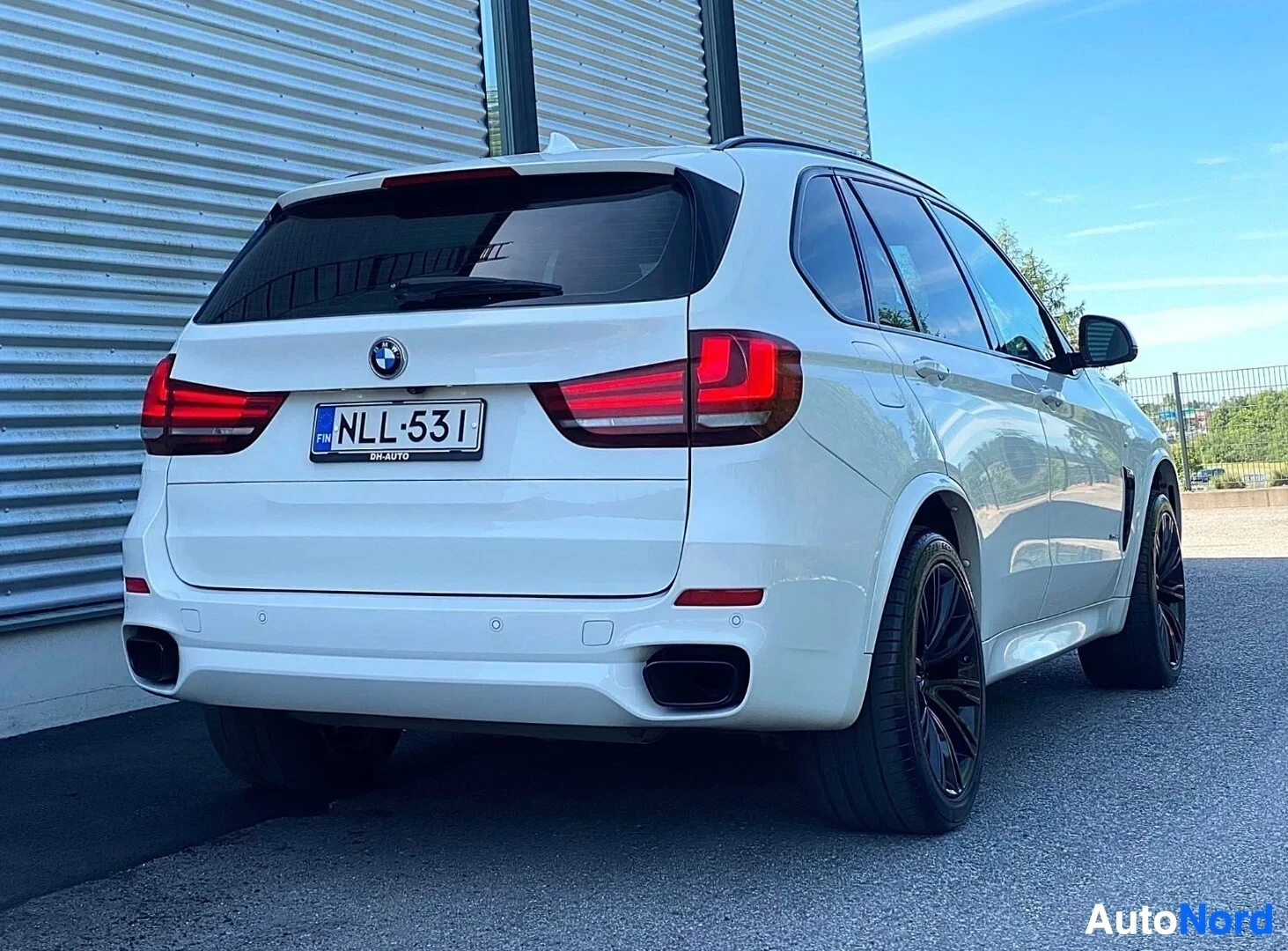 Takaviisto: Valkoinen BMW X5 -maasturi takaviistosta, tummat pyörät, punaisen ja valkean väriset takavalaisimet, rekisterikilvessä