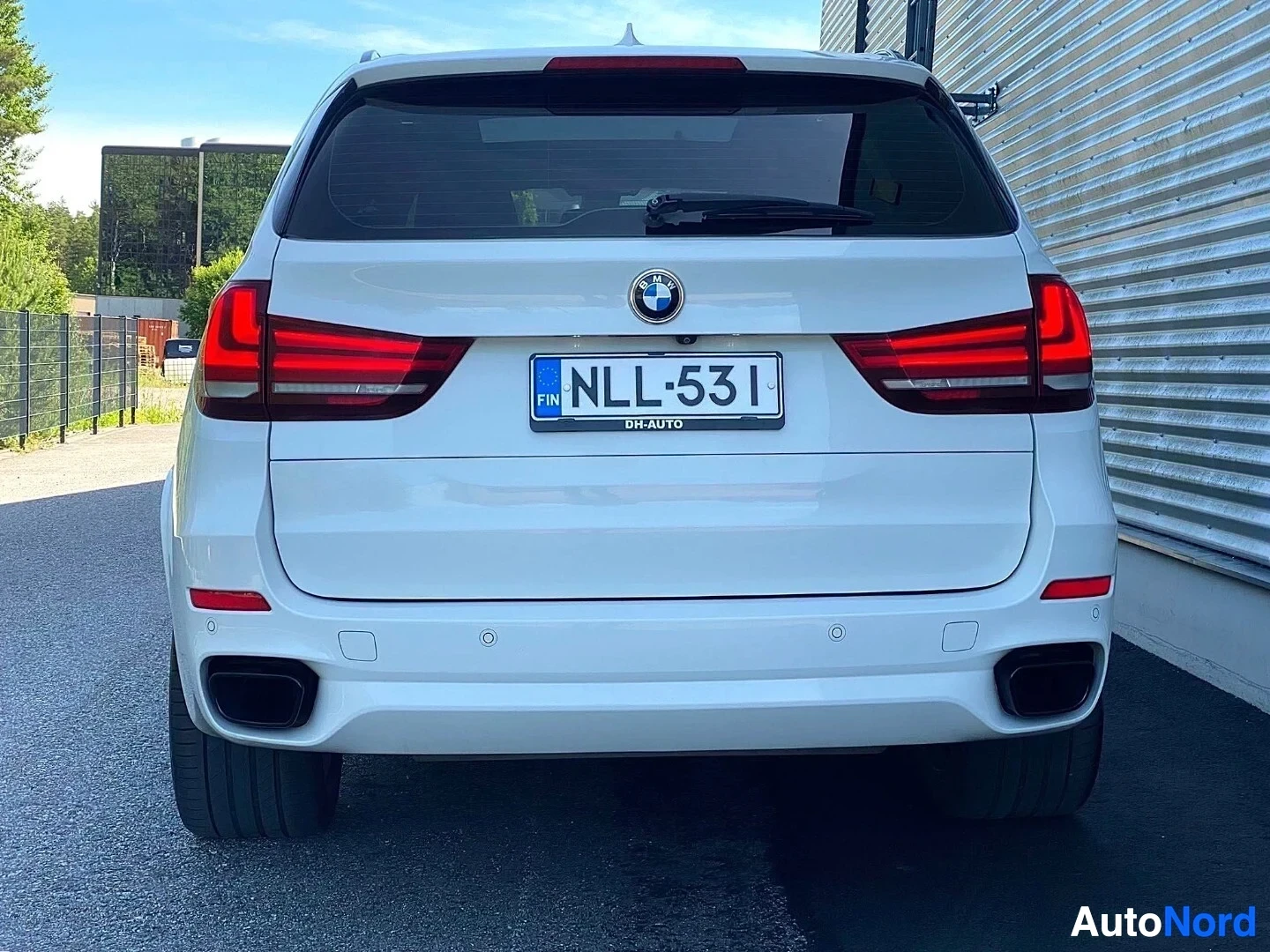 Takaa: Valkoinen BMW X5 -maasturi suoraan takaa kuvattuna, punaisen ja valkean väriset takavalaisimet, rekisterikilvessä, tummat pyörät