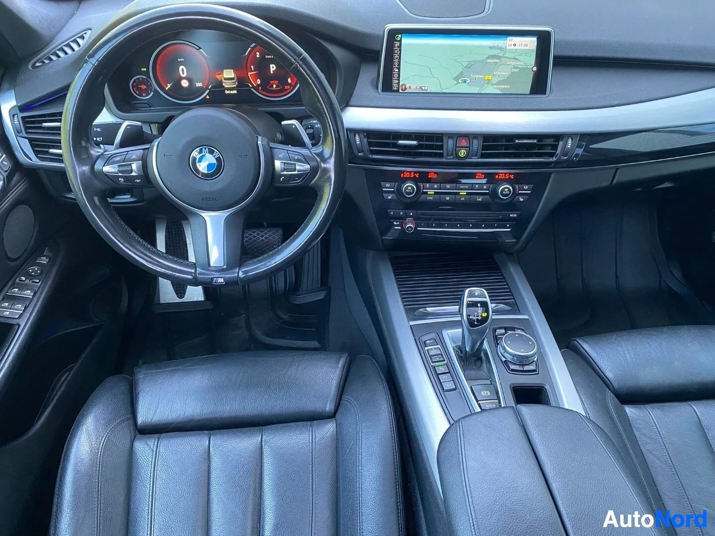 Ohjaamo: Kuljettajapuolen sisätila, ohjauspyörä BMW-logolla, värikäs mittaristopaneeli, näyttö kartta-sovelluksella, keskikonsoli ilmastointi- ja mediaohjauksilla, nahka