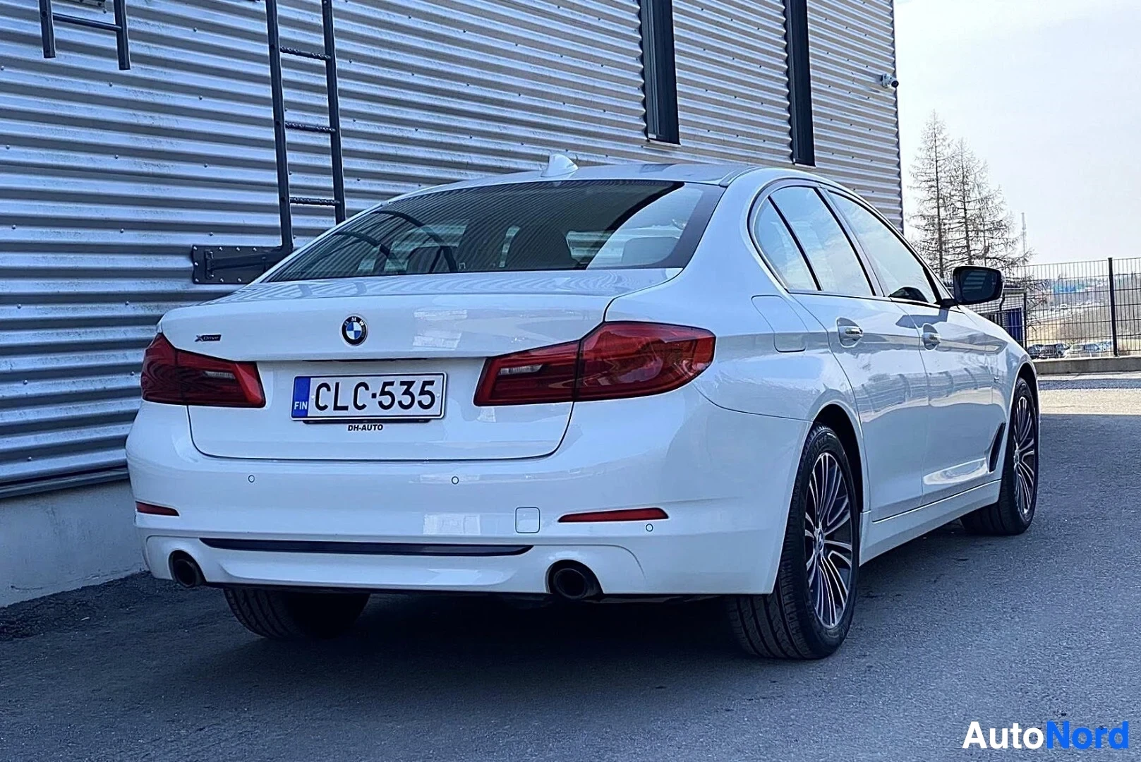 Takaviisto: Valkoinen BMW sedan näkyy takaa kolmen neljänneksen kulmasta. Näkyvissä rekisteritunnus, punaiset takavalot, kaksi pakoputkea, hopeanväriset pyörät ja t