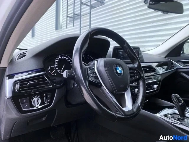 Ohjaamo: Kuljettajan puolen sisätila lähikuvassa: mustainen rattiin merkillä BMW-logolla, mittaristo näkyy, ilmastoinnin ohjauselementit näkyvät.