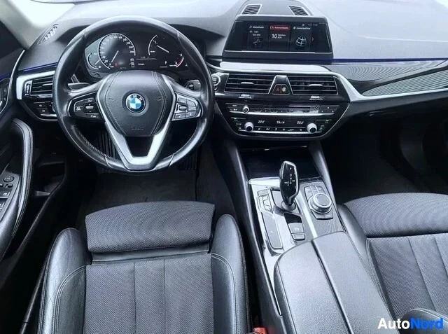 Ohjaamo: BMW G30 auton sisustus edestäpäin. Näkyvät monivärinen ohjauspyörä BMW-logolla, instrumentiklusterit, tumma pääkonsoli ilmastoinnin ohjaimella, digitaalinen näy