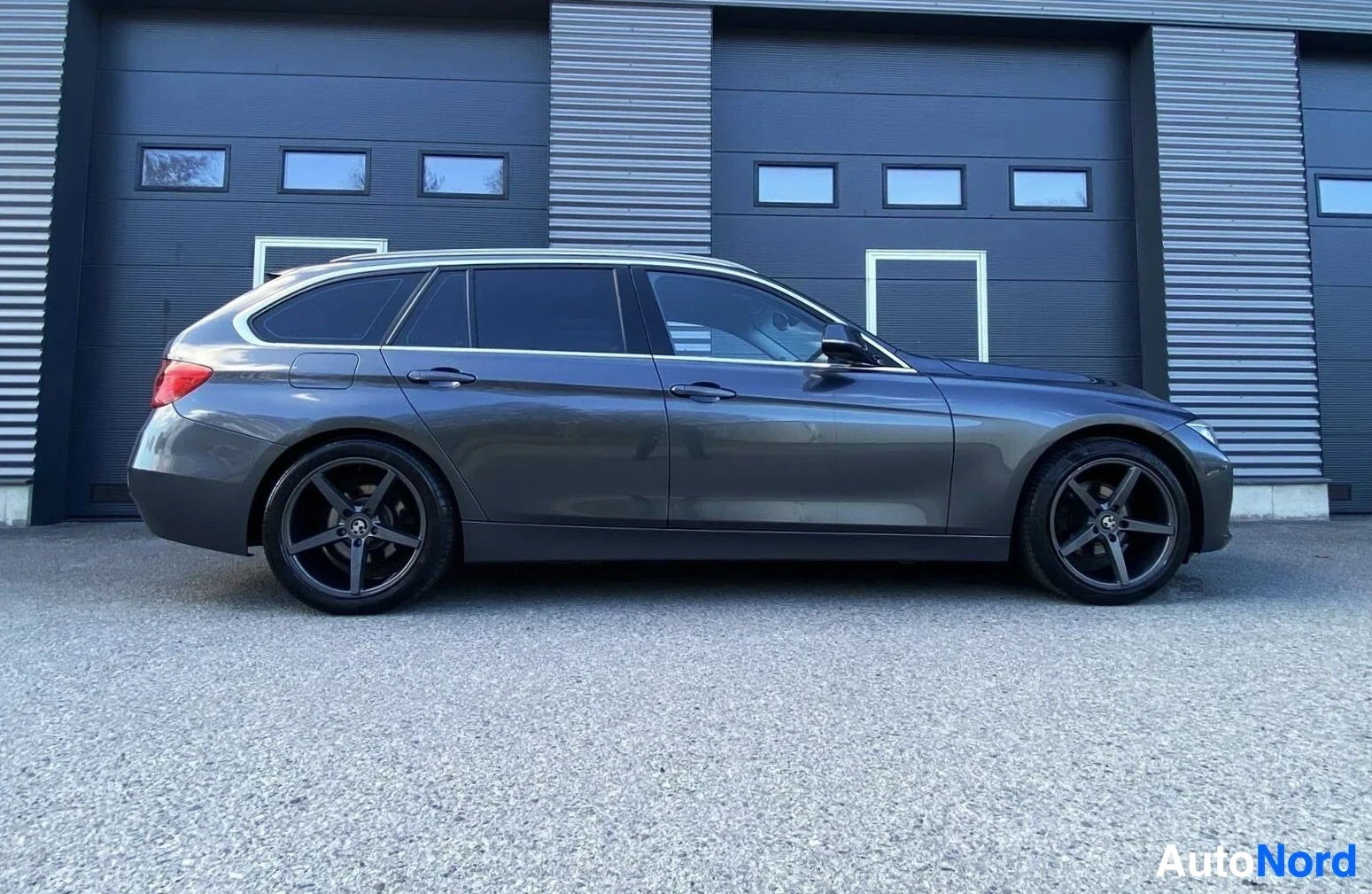 Sivulta: Harmaa BMW-farmari sivusta vasemmalle, tummansinisessä hallissa.