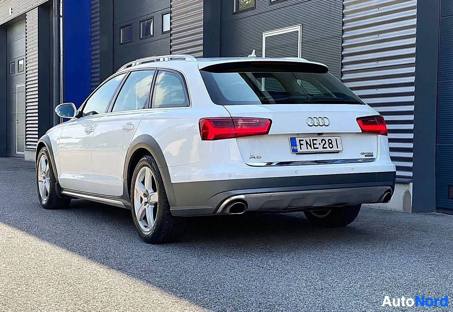 Takaviisto: Valkoinen Audi-farmari kuvattuna kolmen neljänneksen kulmasta takavasemmalta, pysäköitynä teollisuusrakennusten eteen.