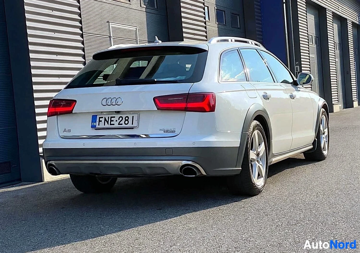 Takaa: Valkoinen Audi-farmari kuvattuna sivulta takaosasta, pysäköitynä teollisuusrakennusten eteen.