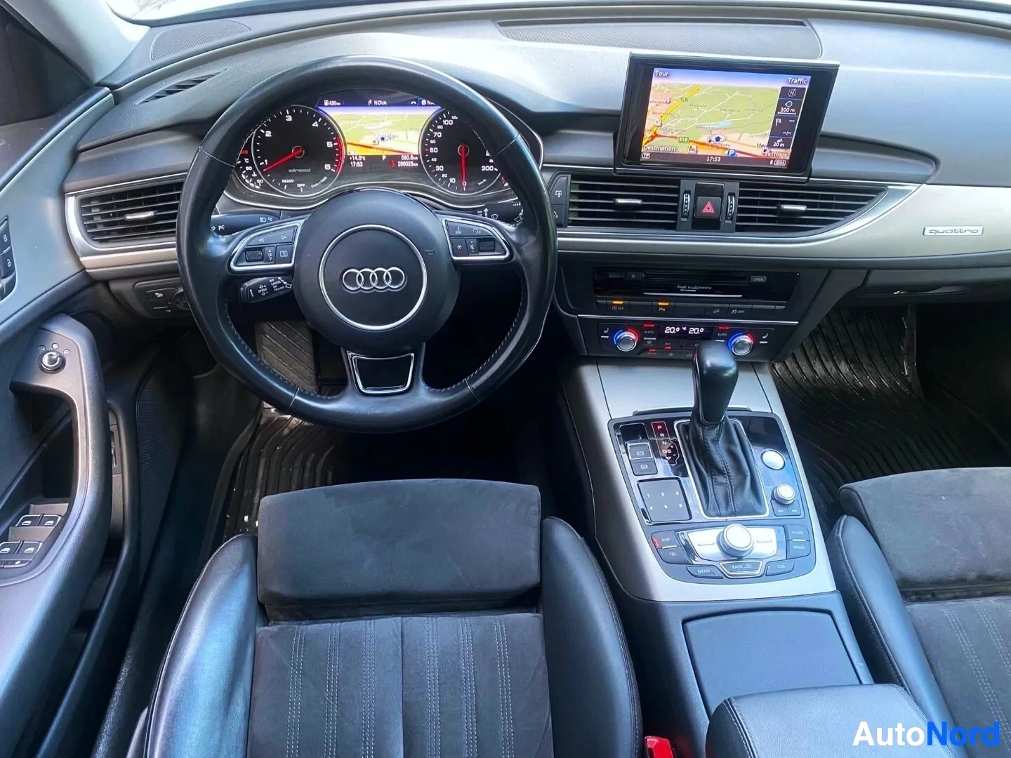 Ohjaamo: Audin ohjaamo edestä kuvattuna. Näkyvät mustavalkoinen ohjauspyörä Audi-logolla, digitaaliset mittarit, navigointilaite oikealla, ilmastoinnin ohjaimet, vaihtei