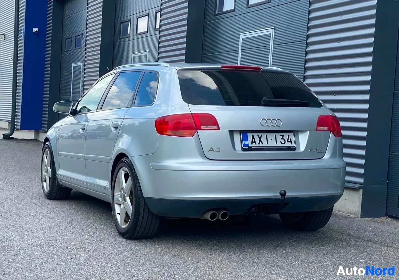 Takaviisto: Hopeinen viistoperä takakulmasta, pysäköity teollisuusrakennusten eteen. Rekisterikilvessä, näkyy Audi-logo ja A3-teksti