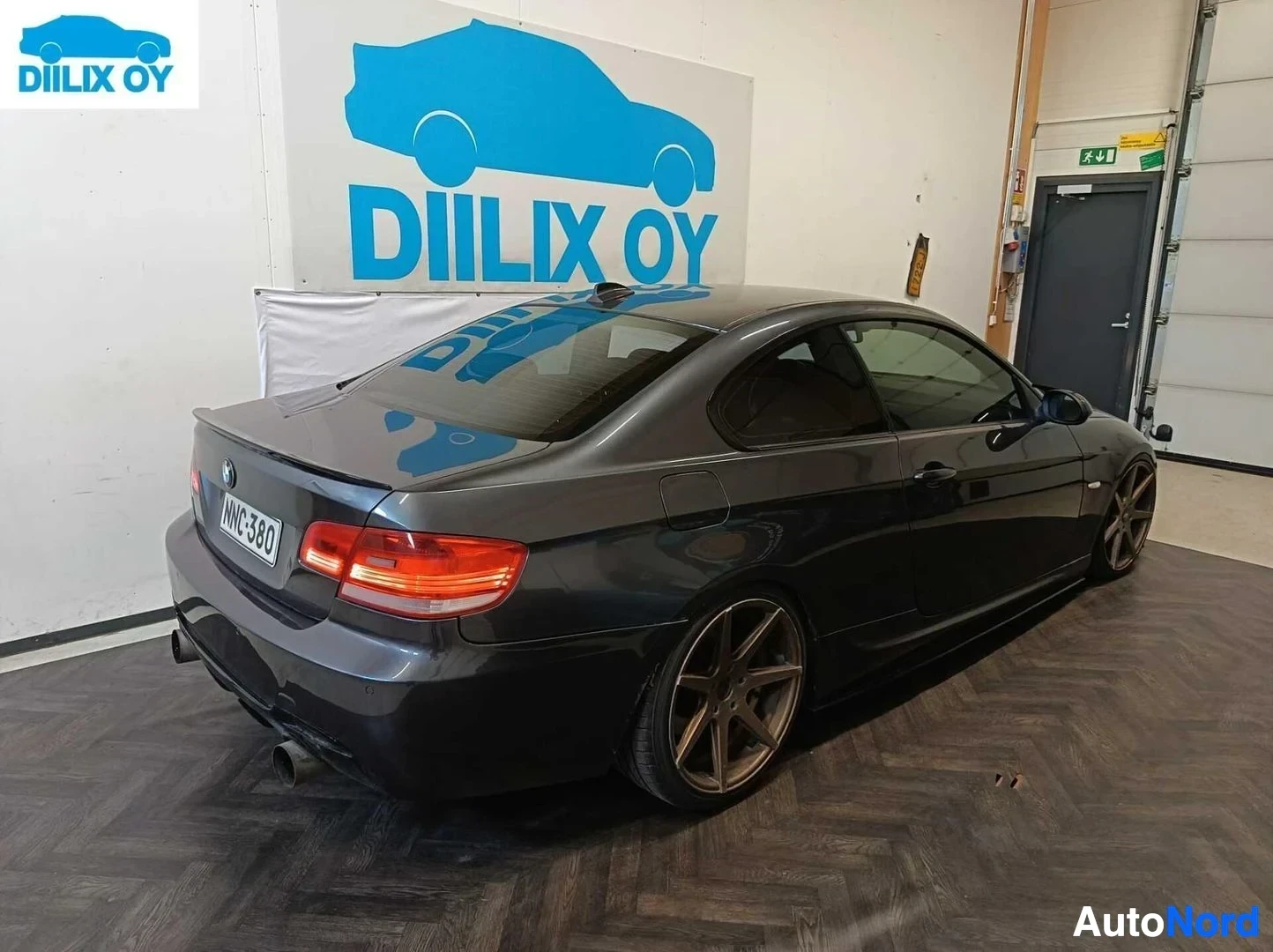 Takaviisto: Musta BMW-coupe takaosasta kuvattuna varikkohallin sisätiloissa. Rekisterikilpi ja punaiset takavalo näkyvät