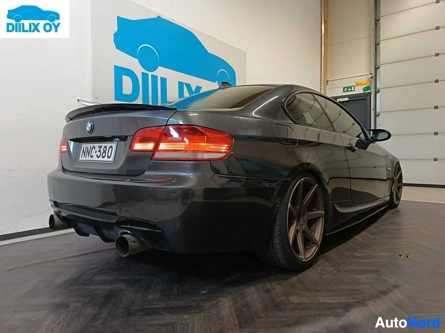 Takaviisto: BMW-sedan sivusta takaapäin katsottuna, tummanvärinen, rekisterikilvessä, metallinen sisäpihalla