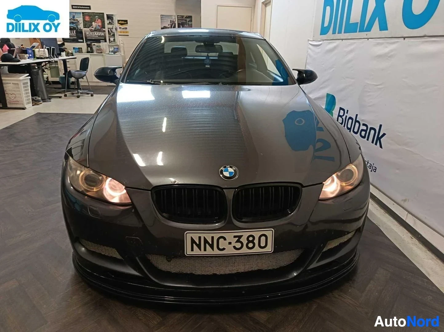 Edestä: BMW-sedan edestä katsottuna, tummanvärinen, rekisterikilvessä, sisäpihalla hallossa