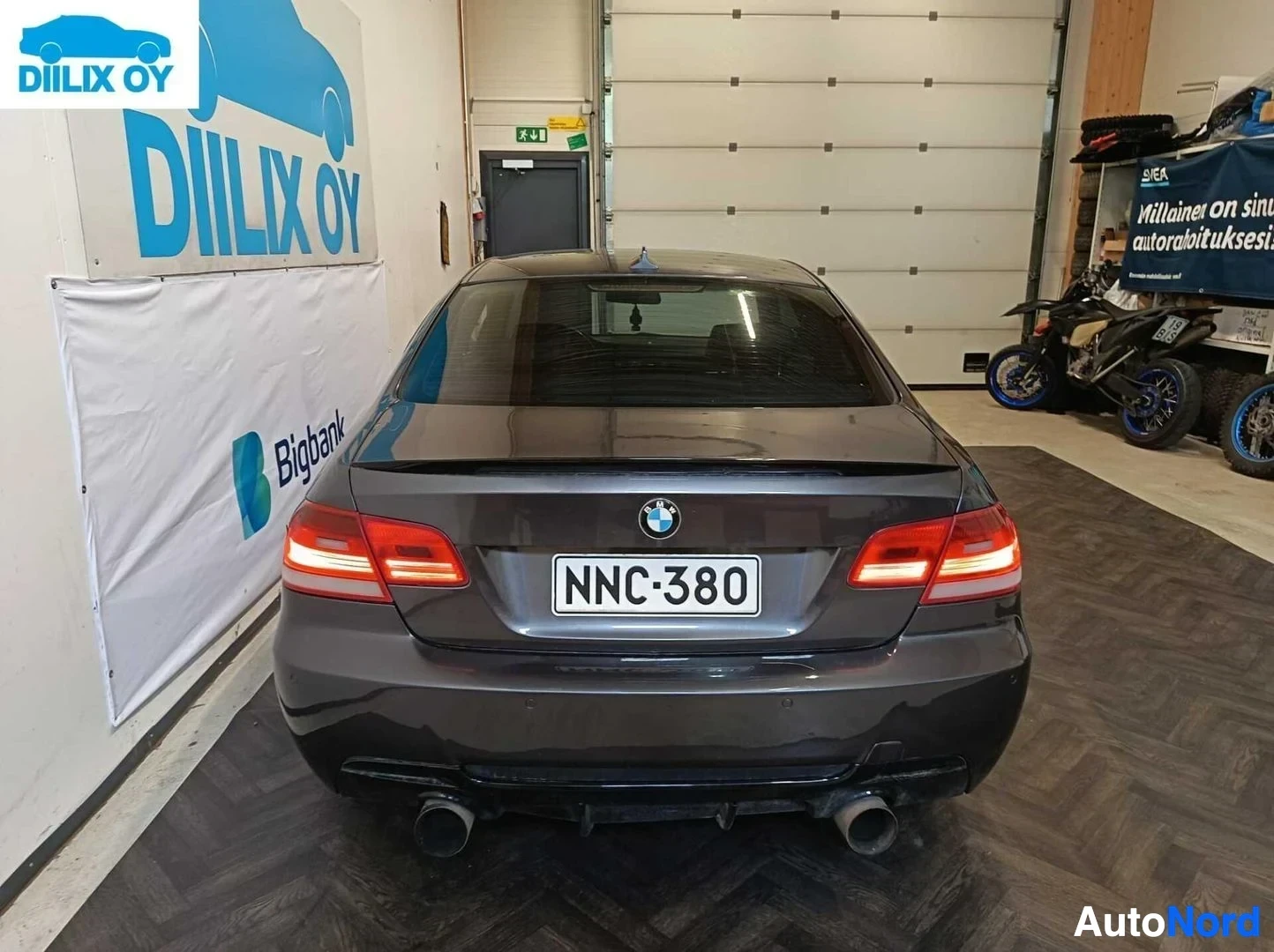 Takaa: BMW 335d M Sport -merkkinen sedan tummansinisen värisellä koriolla, takaosan näkymä, parkkihallissa. Rekisterinumero näkyvissä. Punaset takavalaisimet