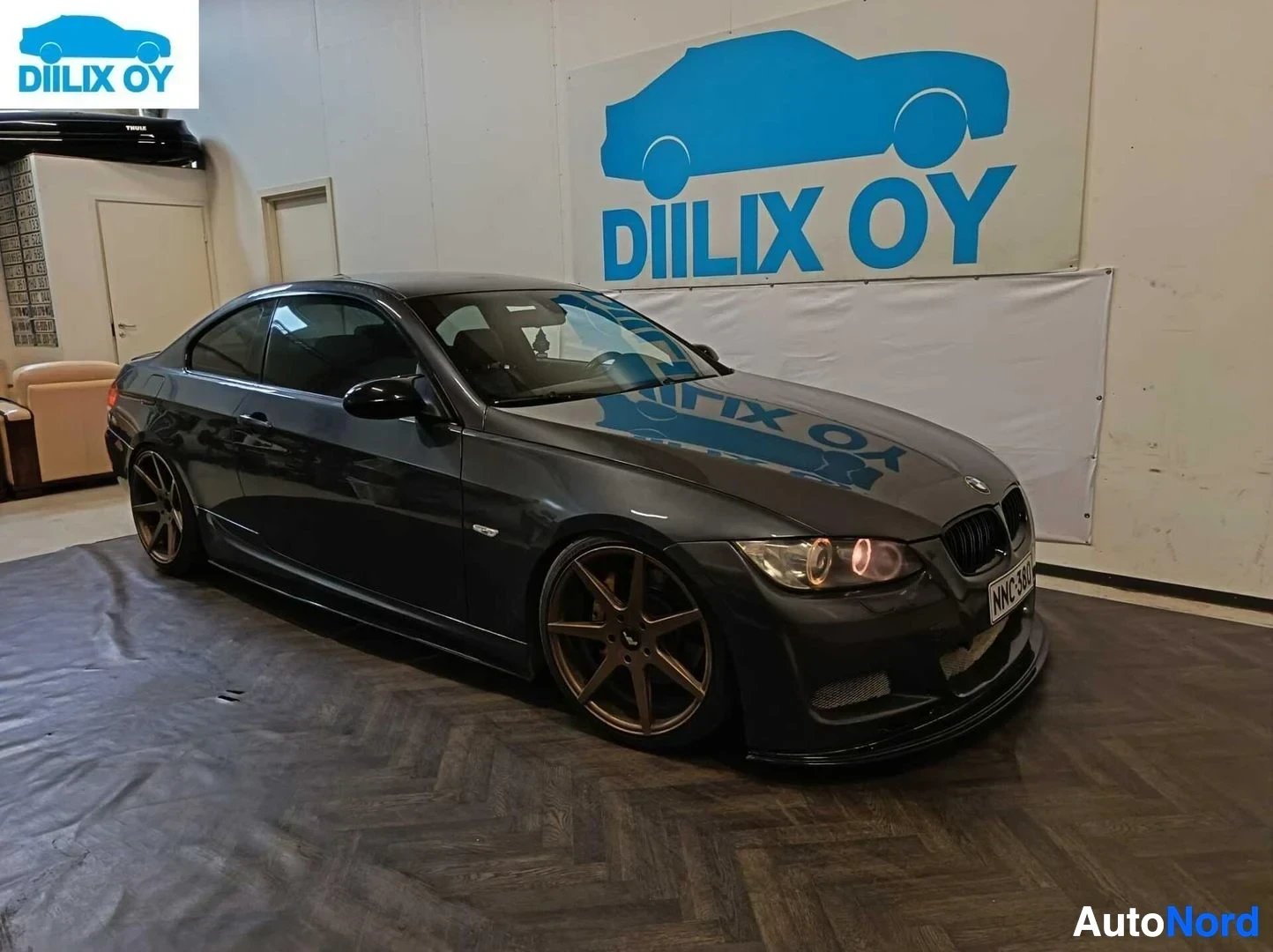 Etuviisto, nokka oikealle: Musta BMW 335 E92 coupe oikealla viistolla, kulta-/pronssinväriset vanteet, punaiset takavalosuulakkeet, näkyvissä rekisterikyltti