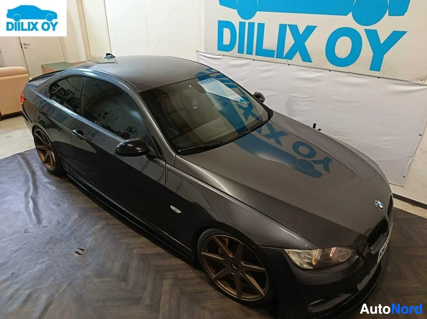 Etuviisto: Musta BMW 335 E92 coupe ylhäältä kuvattu, kulta-/pronssinväriset vanteet, katto- ja sivupinnat näkyvät, varaston taustakangas