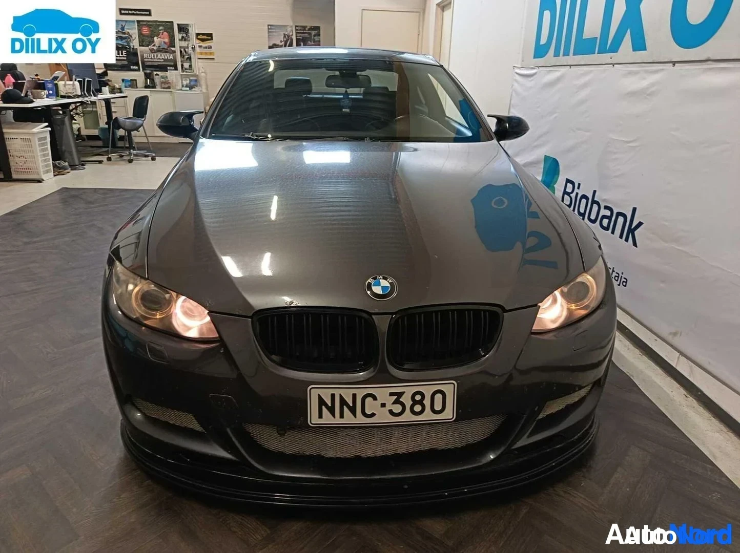 Edestä: Tummanharmaa BMW 3-sarjan coupé suoraan edestä kuvattuna, edessä rekisterikilpi '', musta etusäleikkö ja etuspoileri.