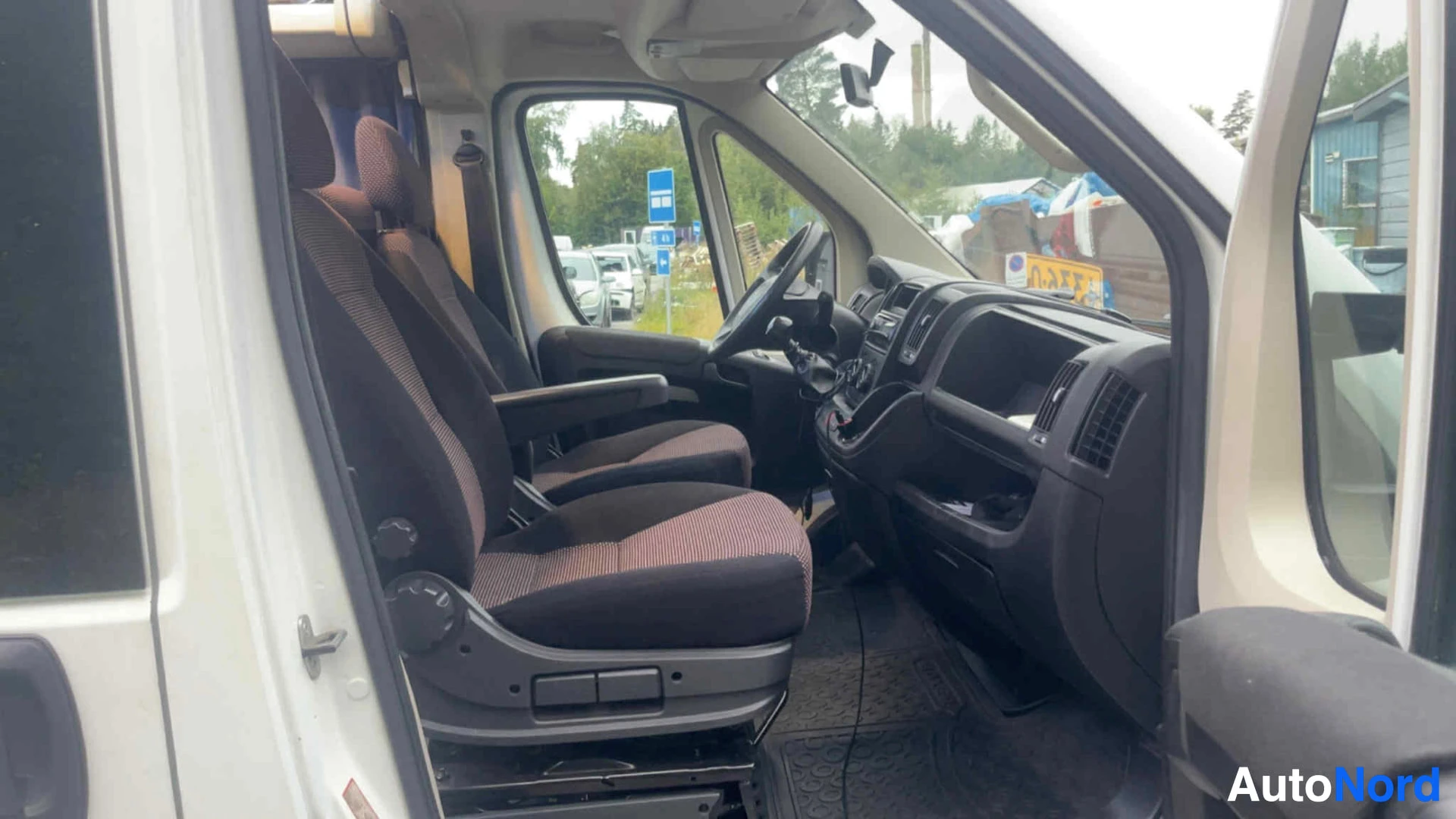 Ohjaamo: Pakettiauto ohjaamosta sisältä näkymässä. Kaksi etupaikka: kuljettajapaikka vasemmalla ja matkustajapaikka oikealla, molemmat ruskeilla tekstiileillä verhoillui