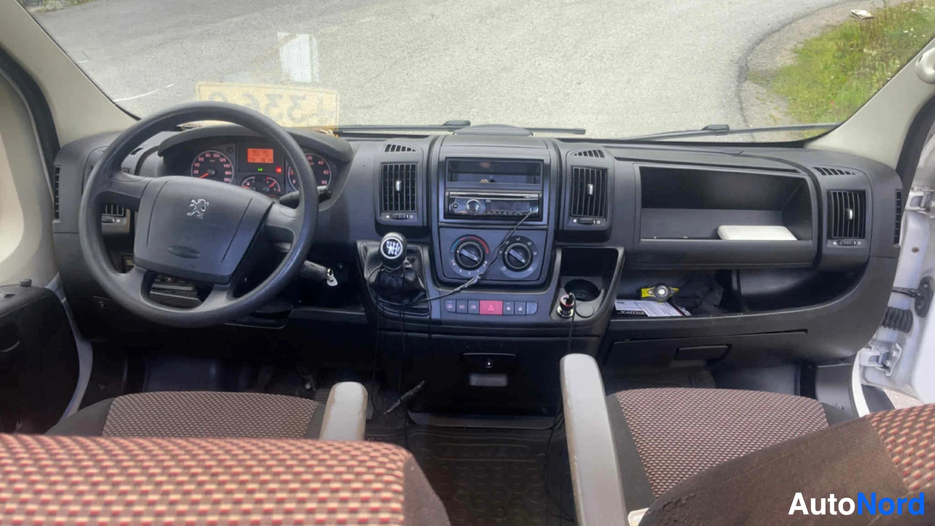 Etuistuimet: Kuljettajan näkökulma ohjauspyörään ja instrumenttilautaan; Peugeot-logo näkyvissä, radio-CD-soitin ja ilmastointi-ohjaimet.