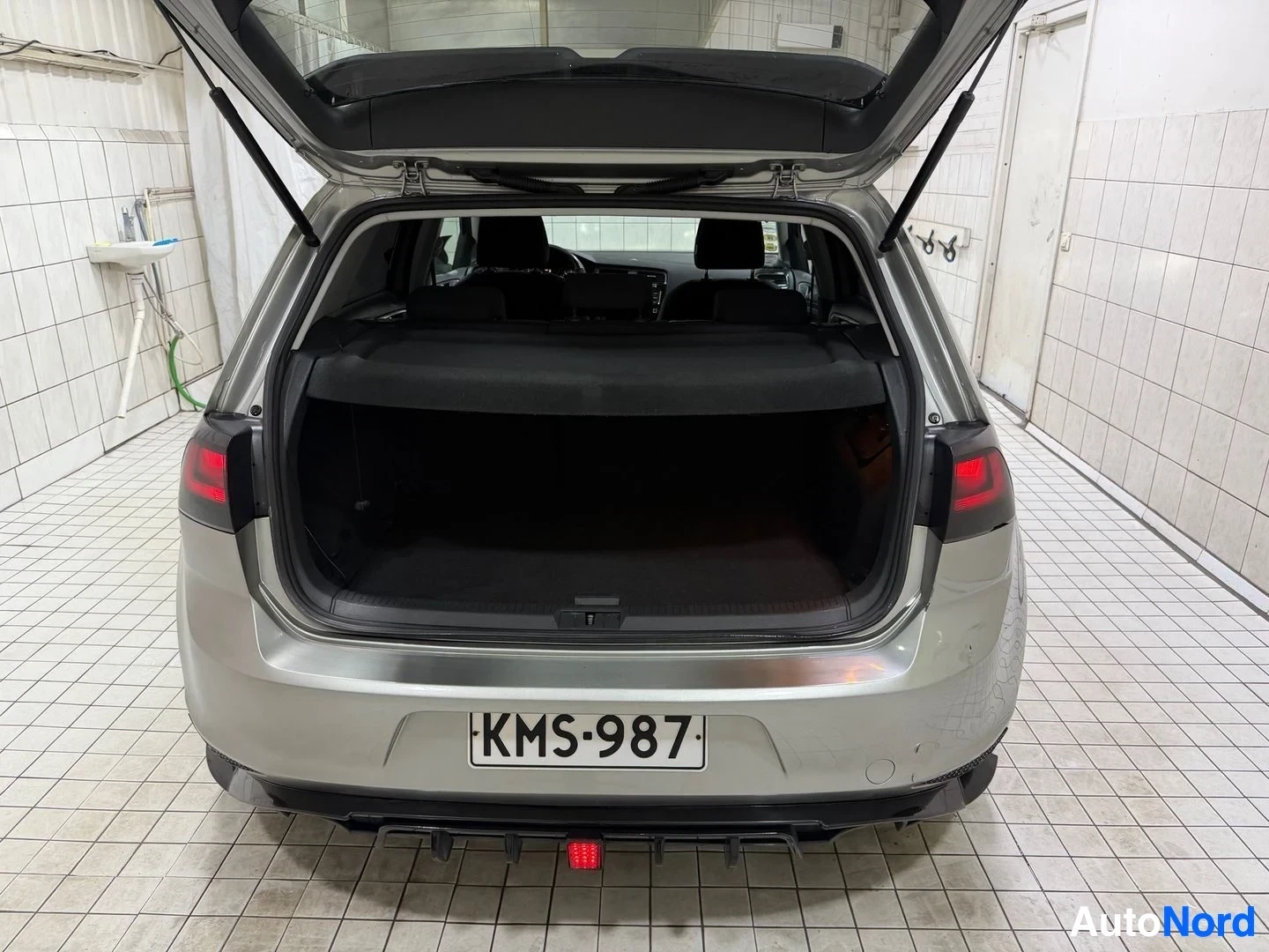 Tavaratila: Volkswagen Golf avatulla takaluukulla hallissa, kuvattu suoraan takaa. Näkyy tumma lastipinta, rekisteritunnus ja halliseinät