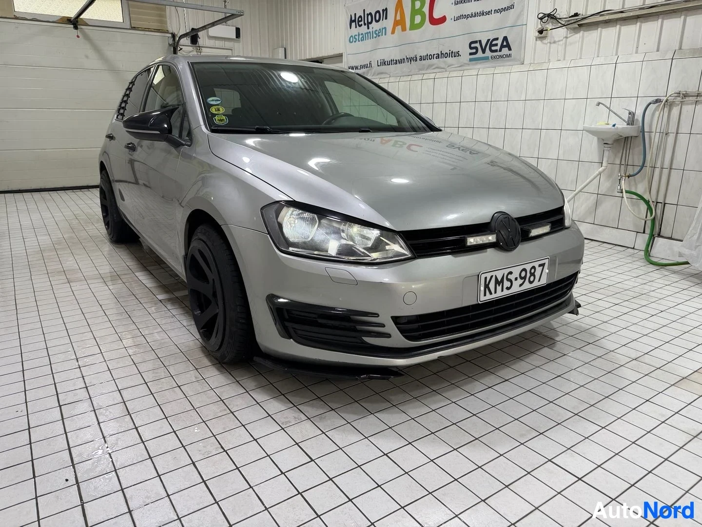 Edestä: Hopeinen viisioviinen Volkswagen Golf-henkilöauto etuosasta kuvattuna hallin sisällä. Rekisterikilvessä. Mustat johdekaaret, mustat sivupeilit. LED-sisä