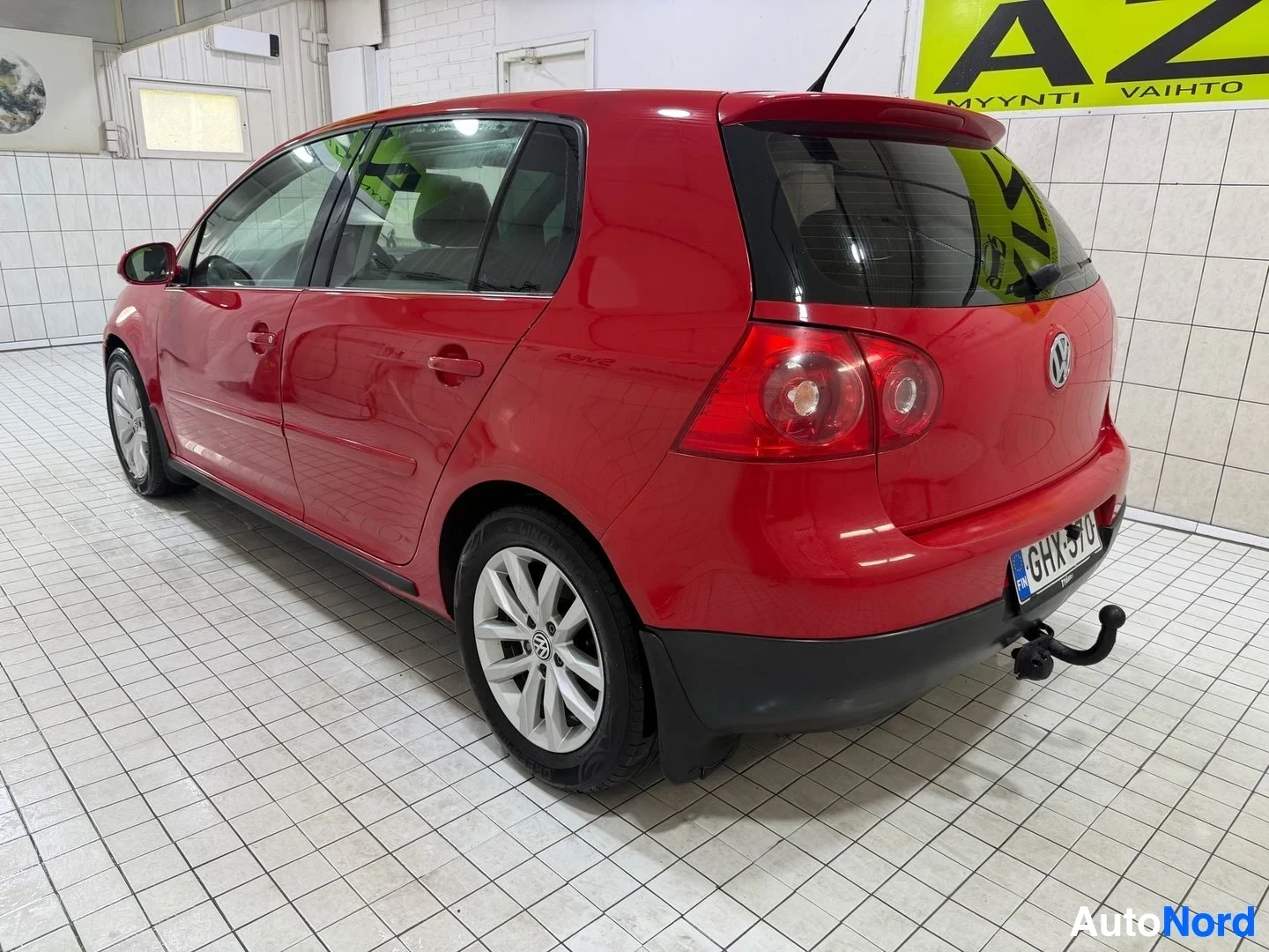 Takaviisto: Punainen Volkswagen Golf -henkilöauto kuvattu takaa oikealla puolella hallissa. Auton taka-akselit ja takalampuista näkyvät selvästi.