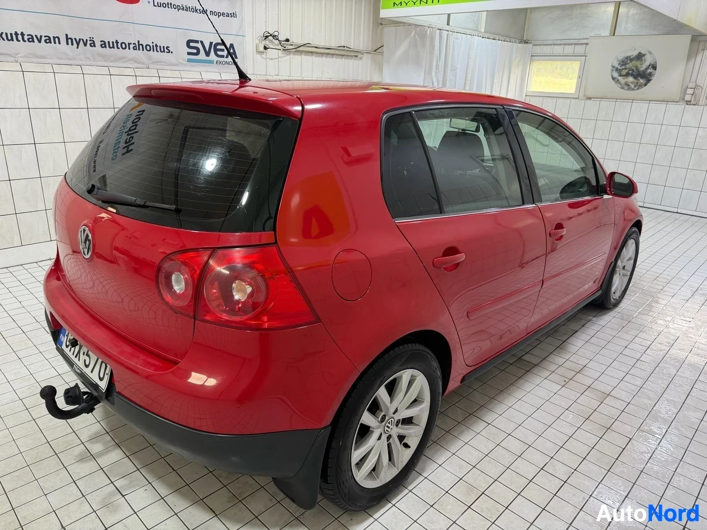 Takaviisto: Punainen Volkswagen Golf -henkilöauto kuvattu takaa hieman oikealta, hallissa. Auton taka-akselit, takalampuista ja vetolaitteen kiinnike näkyvät.