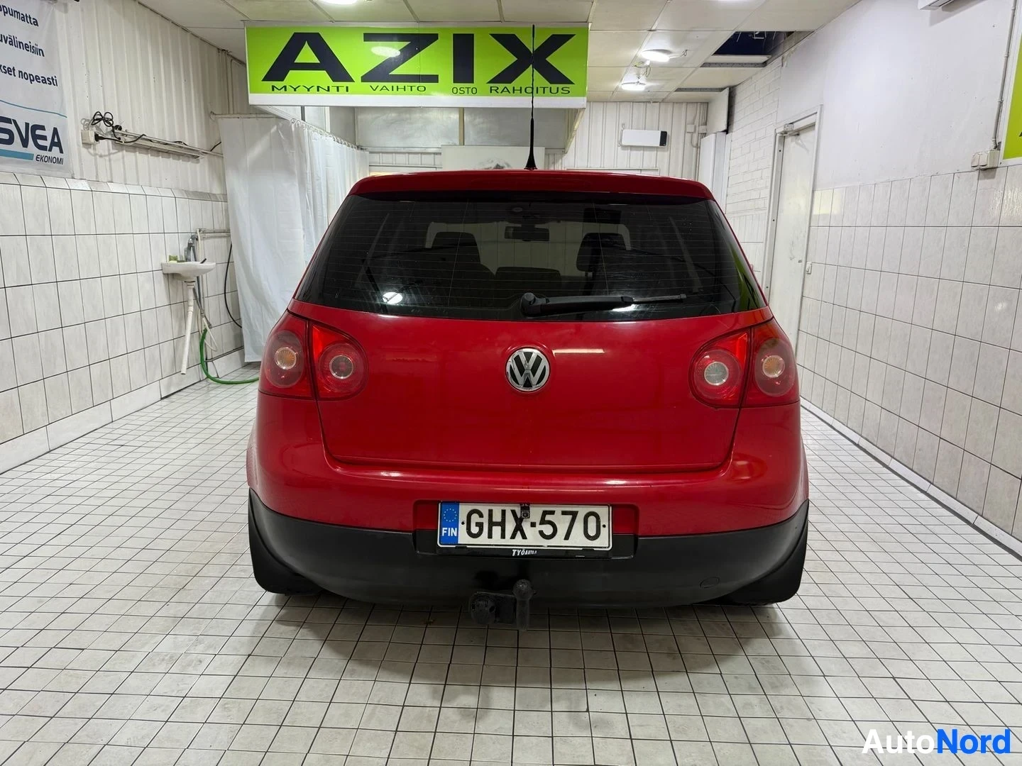 Takaa: Punainen Volkswagen Golf seisoo sisätiloissa takaapäin kuvattuna. Rekisterikilpi on näkyvissä. Takalokasuoja, takavalot ja tummennetu takaikkunan lasi o