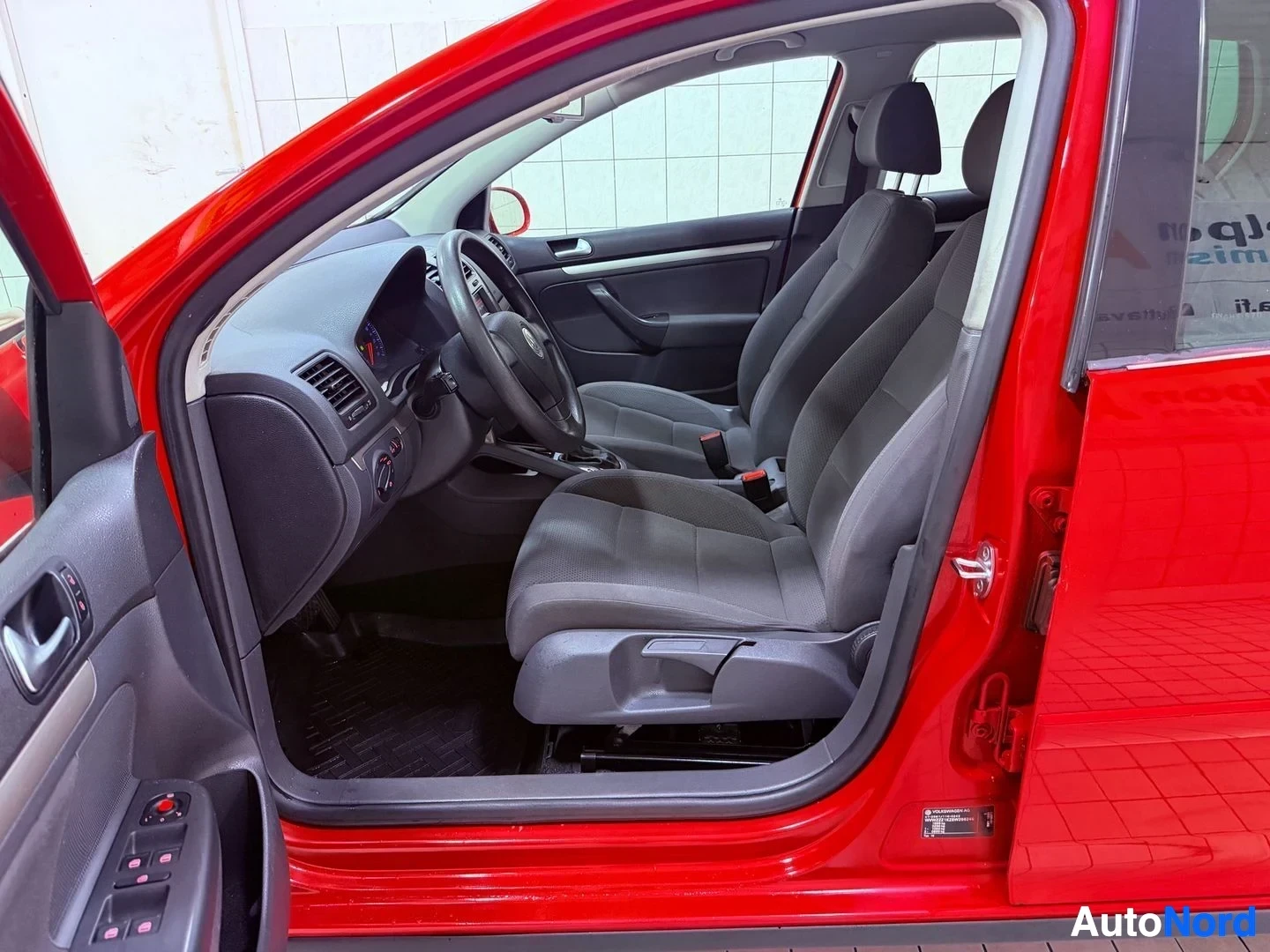 Etuistuimet: Punaisen Volkswagen Golf -auton etupenkki, kuljettajan puoli, sisältäen ohjauspyörän ja hallintalaitteet, näkymä avoimesta ovesta