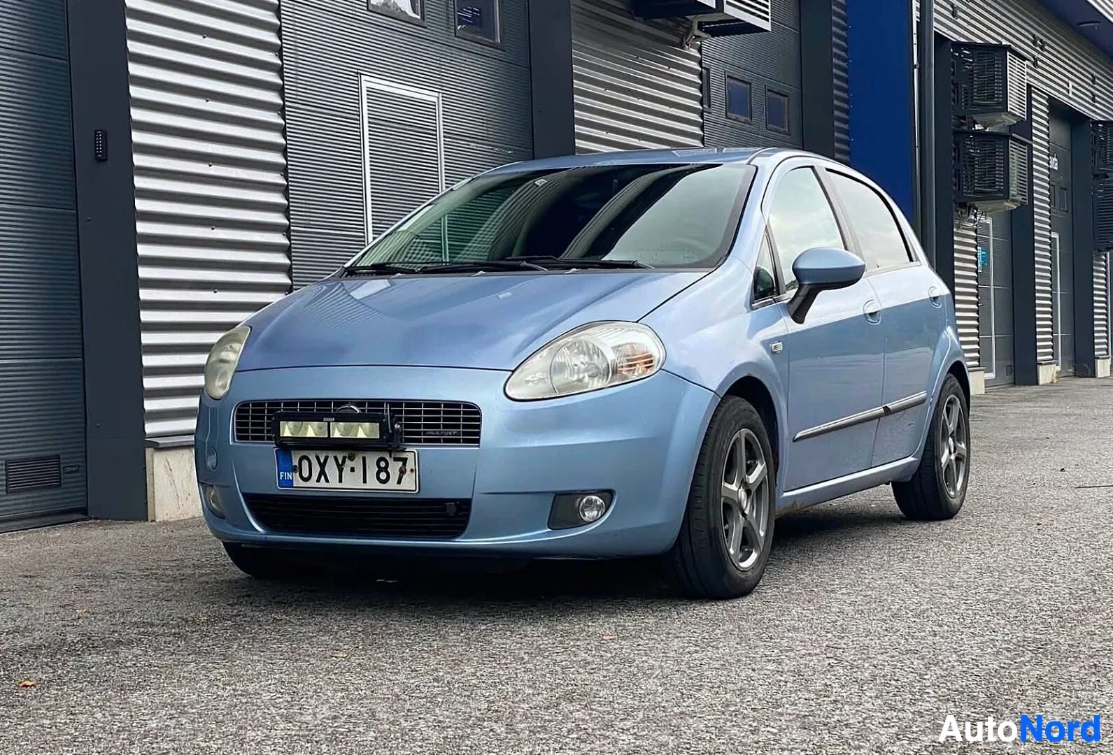 Etuviisto, nokka vasemmalle: Vaaleansininen Fiat Grande Punto, etunäkymä hieman vasemmalle, rekisterinumero näkyvissä