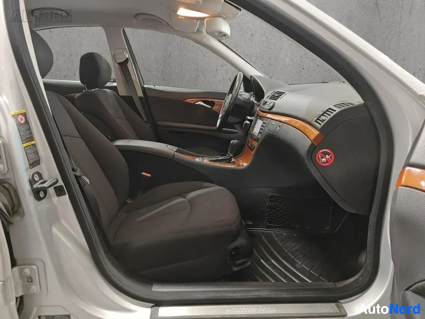 Etuistuimet: Mercedes-Benz E etupenkki vasemmalta: mustalla verhoilulla varustettu kuljettajan istuimen sivu, ratti, puuinteriööri, oranssit ilmanvaihdon suuaukot ja mustat