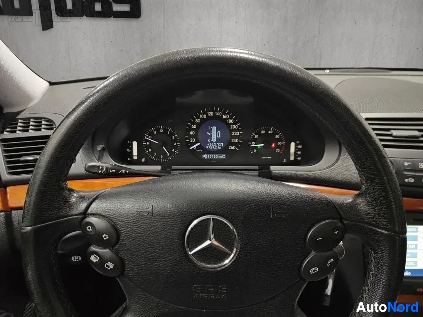 Yksityiskohta: Lähikuva Mercedes-Benz instrumentoinnista: mittaristo näyttää noin 97 252 km ajomatkaa ja muita lukemia, oranssimusta puuinteriööri, musta nahkaratti ja merkinn