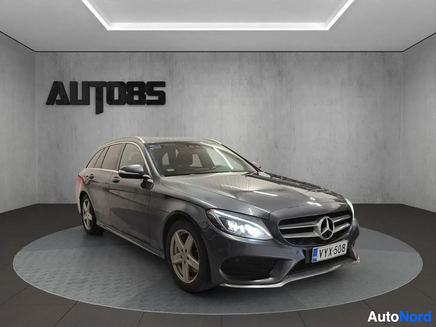 Etuviisto, nokka vasemmalle: Mercedes-Benz sedan, harmaa väri, kolmitonäkymä vasemmalle, valkoisen katon showroomissa