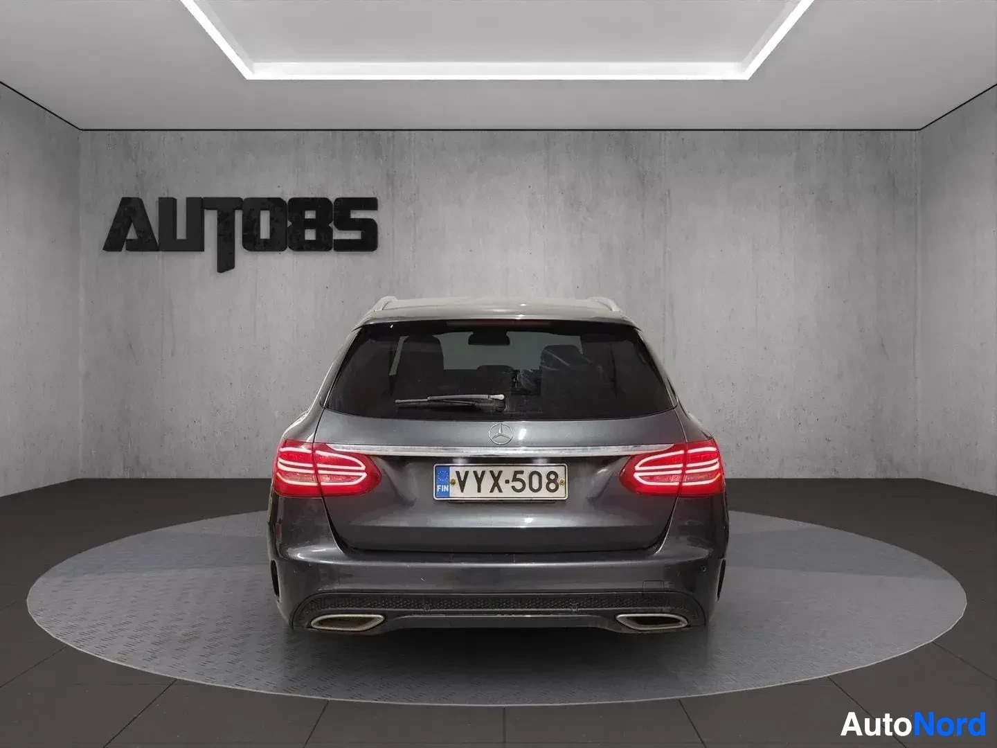 Takaa: Harmaa Mercedes-Benz estate-auto kuvattuna takaa, punaiset takavalon yksiköt näkyvissä, rekisterikilpi näkyvissä, kaksi pakoputkea näkyvissä
