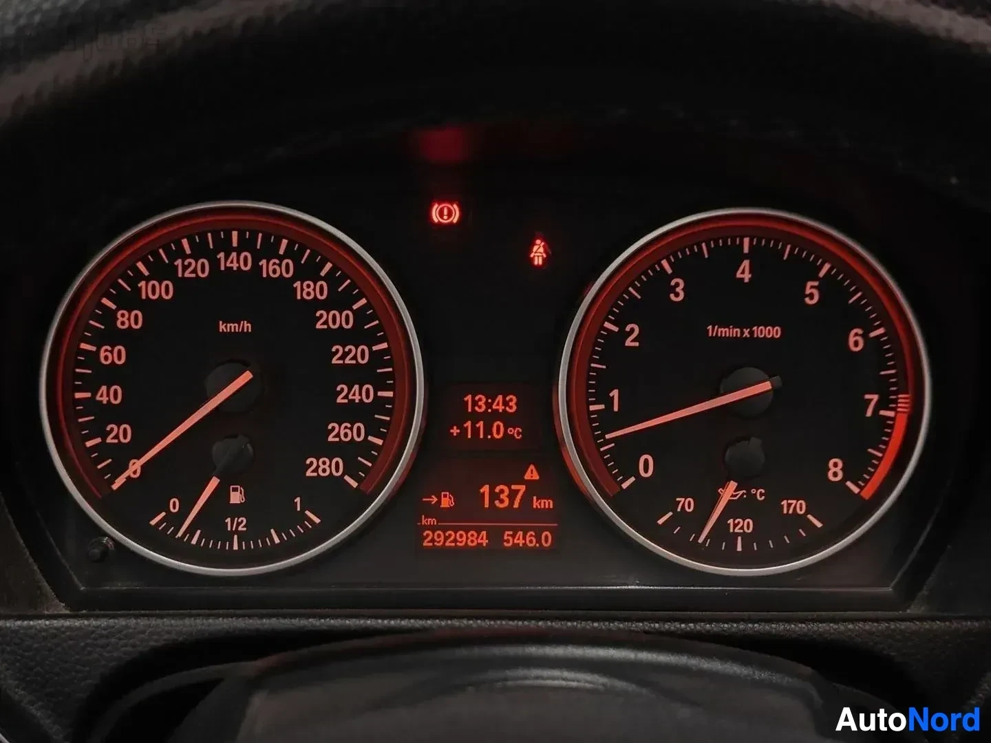 Yksityiskohta: Mittaritaulu punaisella valaistuksella, vasemmalla nopeusmittari 0-280 km/h, oikealla kierrosluvun mittari, keskeisellä näytöllä 13:43, +11,0°C, 137 km jäljellä