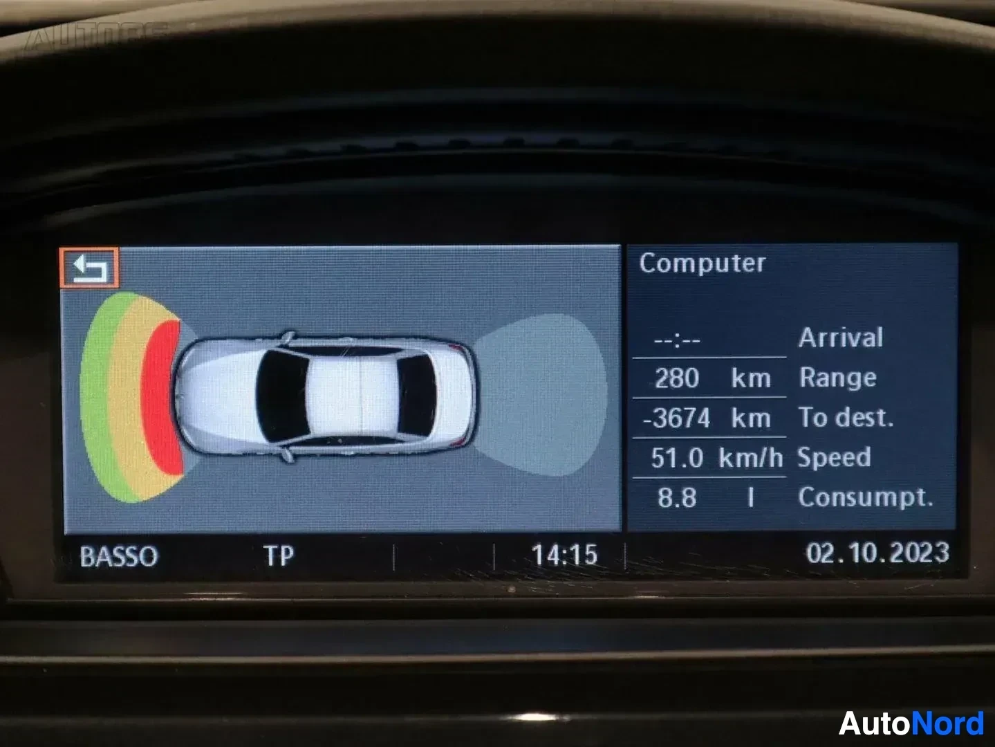 Ohjaamo: Auton sisänäkymä: parkeeriavustimen grafiikka näytössä, etäisyys-sensorien näyttö punaisella ja keltaisella väreillä.
