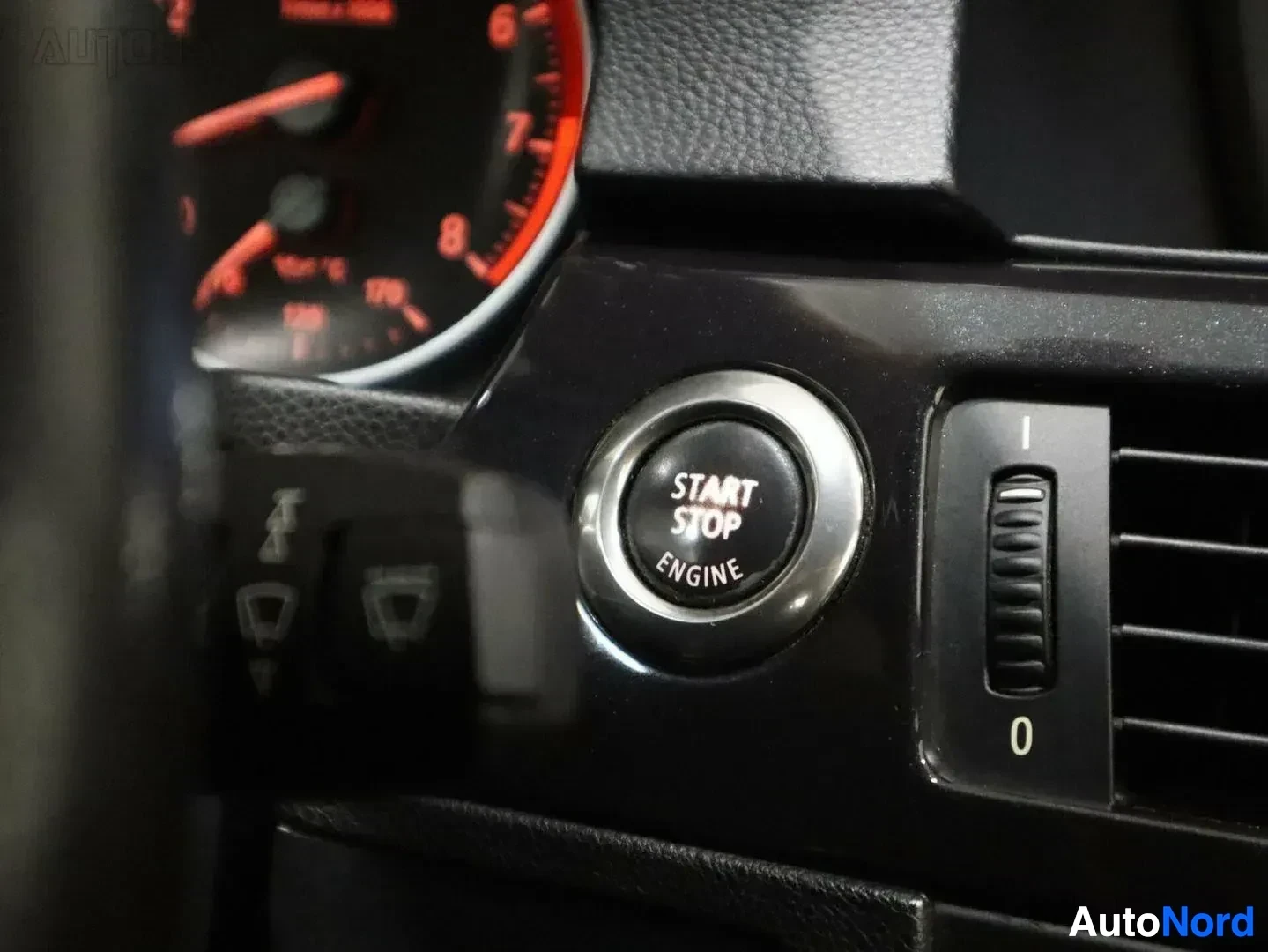 Yksityiskohta: Auton sisänäkymä: Start Stop Engine -painike ja ilmastointi-ohjain lähikuvassa, vasemmalla mittaristo punaisella valaistuksella.
