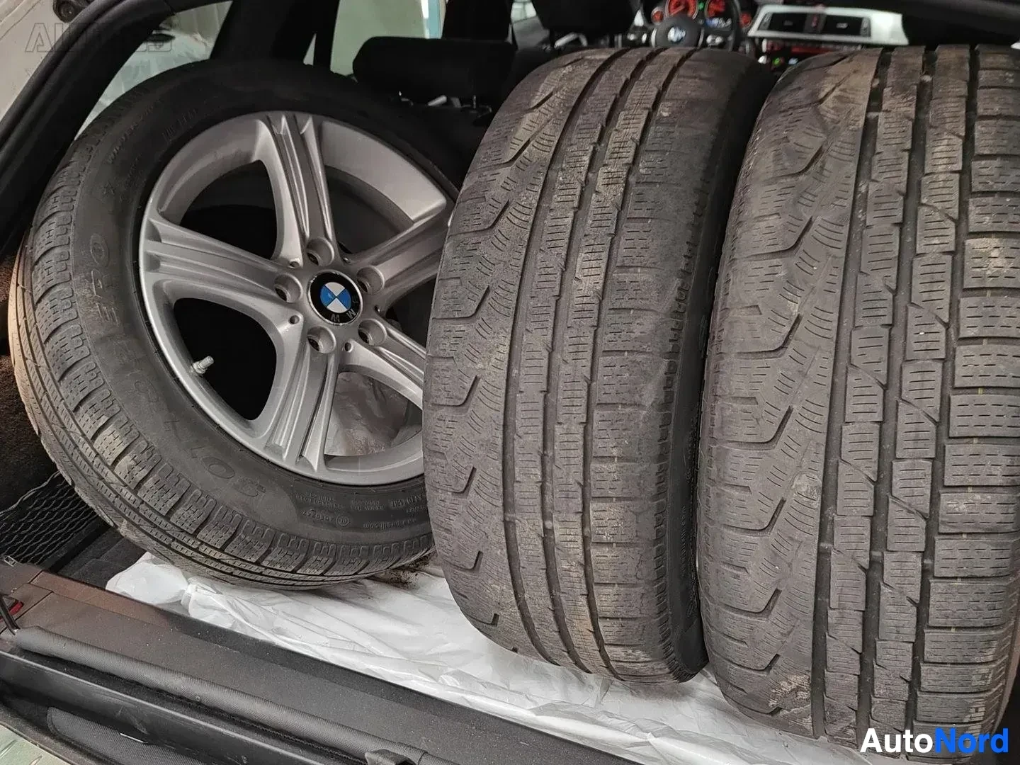 Yksityiskohta: Neljä renkaita rivissä, yksi BMW-vantteella vasemmalla. Kolme rengasta tuntemattomilla merkinnöillä ja pinnalla näkyviä kulumisjälkiä. Renkaiden pinnat näyttävä
