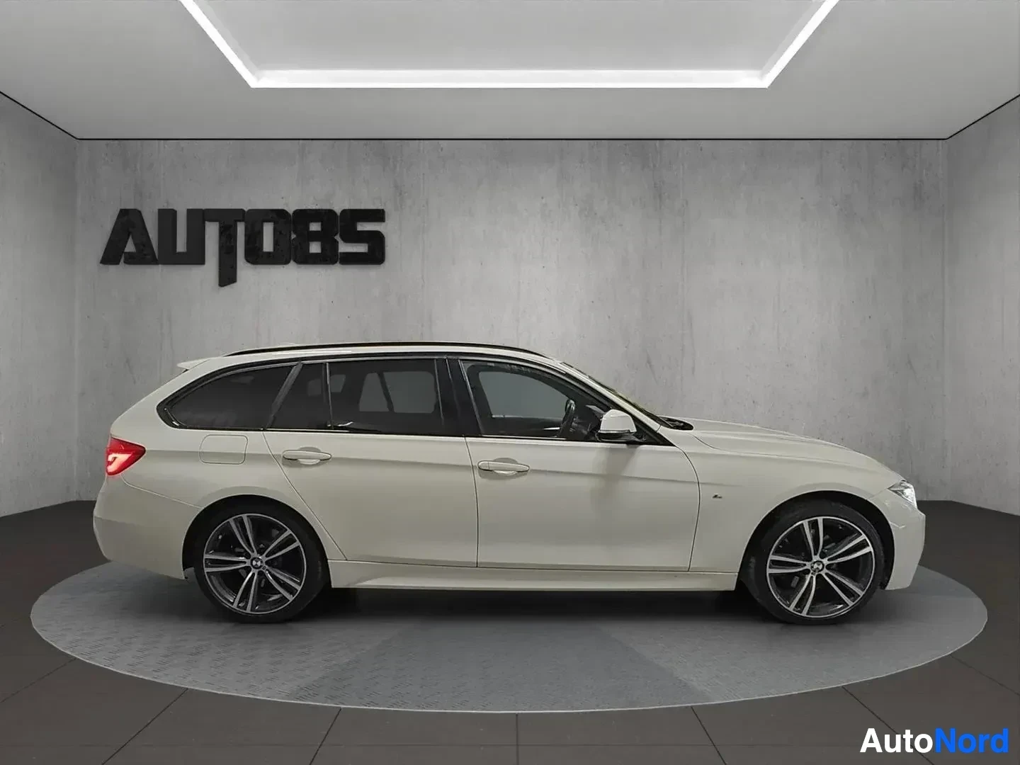 Sivulta: Valkoinen BMW 330 Touring sivusta oikealle kuvattuna näyttelytilassa, koko ajoneuvon sivuprofiili näkyvissä.