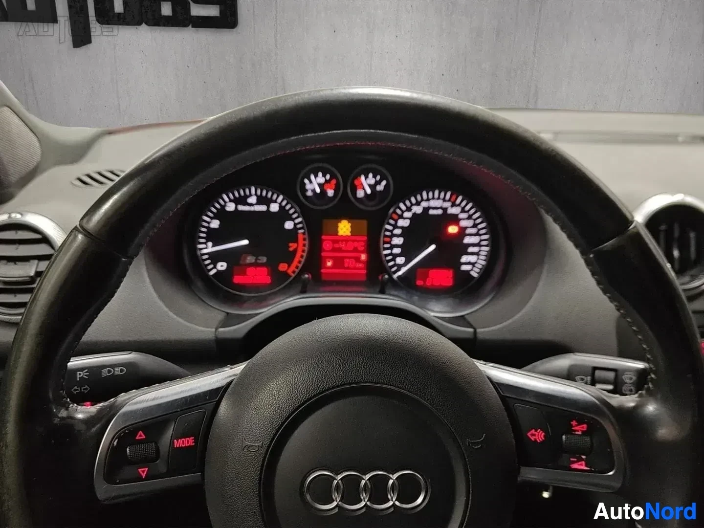 Yksityiskohta: Audin mittaristopaneeli ja ohjauspyörä, analogiavärit näkyvät ja Audi-logo ohjauspyörän keskellä.