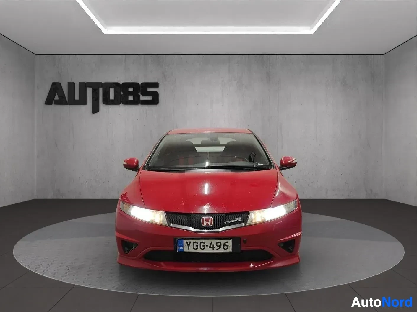 Edestä: Punainen Honda Civic -kupeista auto näytetään suoraan edestä. Auto on valaistussa näyttelytilassa AUTO85-merkillä taustalla. Rekisterikilpi näkyy selvästi.