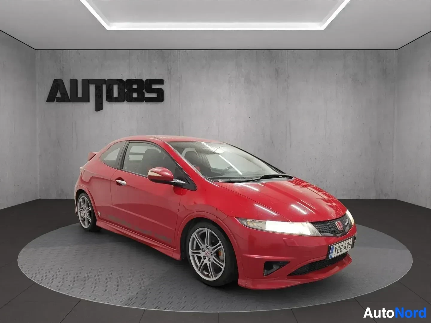 Etuviisto, nokka oikealle: Punainen Honda Civic -kupeista auto näytetään kolmesta neljäsosasta oikealle. Auto on valaistussa näyttelytilassa AUTO85-merkillä taustalla.