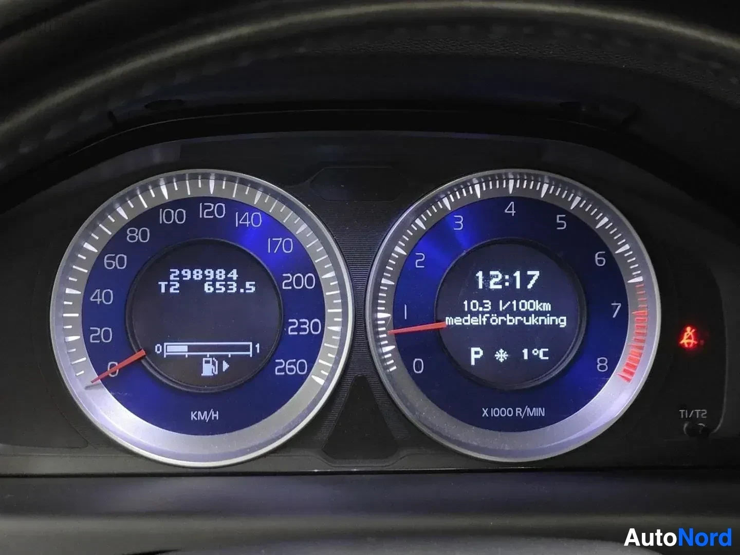Yksityiskohta: Lähikuva Volvo auton digitaalisesta mittaristosta, näyttää 298984 km ajokilometriä, kellonaikaa 12:17, polttoaineen kulutus ja moottoriyksikön tiedot näkyvillä.