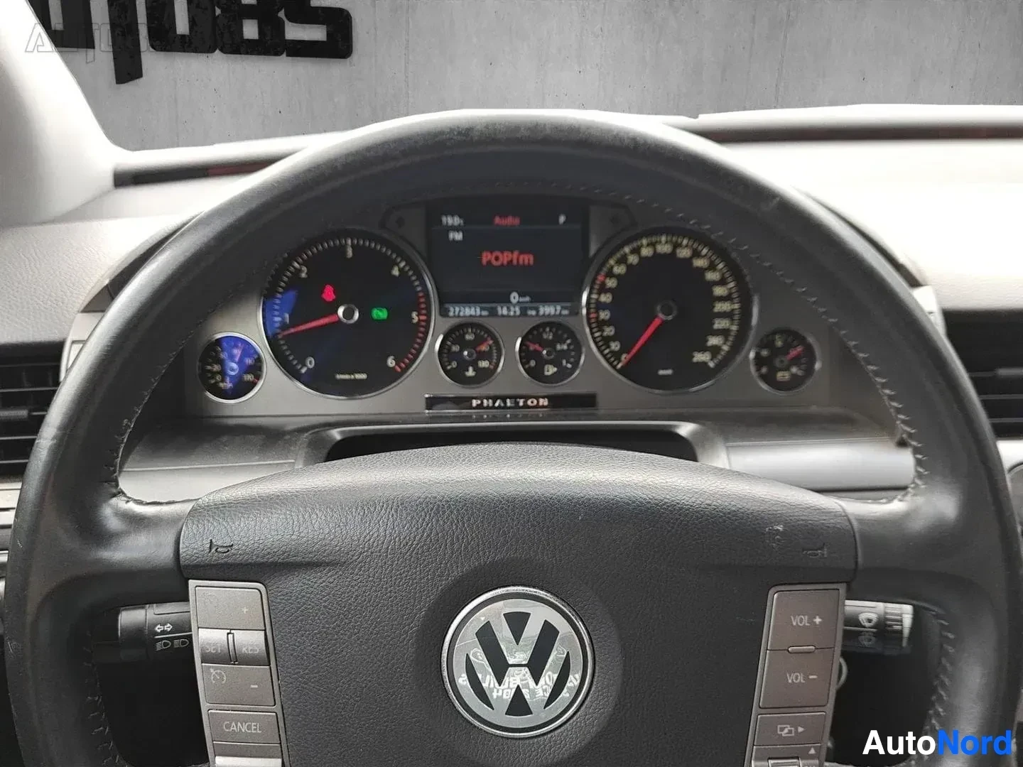 Yksityiskohta: Mittaristonäyttö lähikuvassa, POPfm näyttö, kolmilukemät mittarit, PHAETON teksti mittariston yläosassa, Volkswagen-logo ohjauratilla