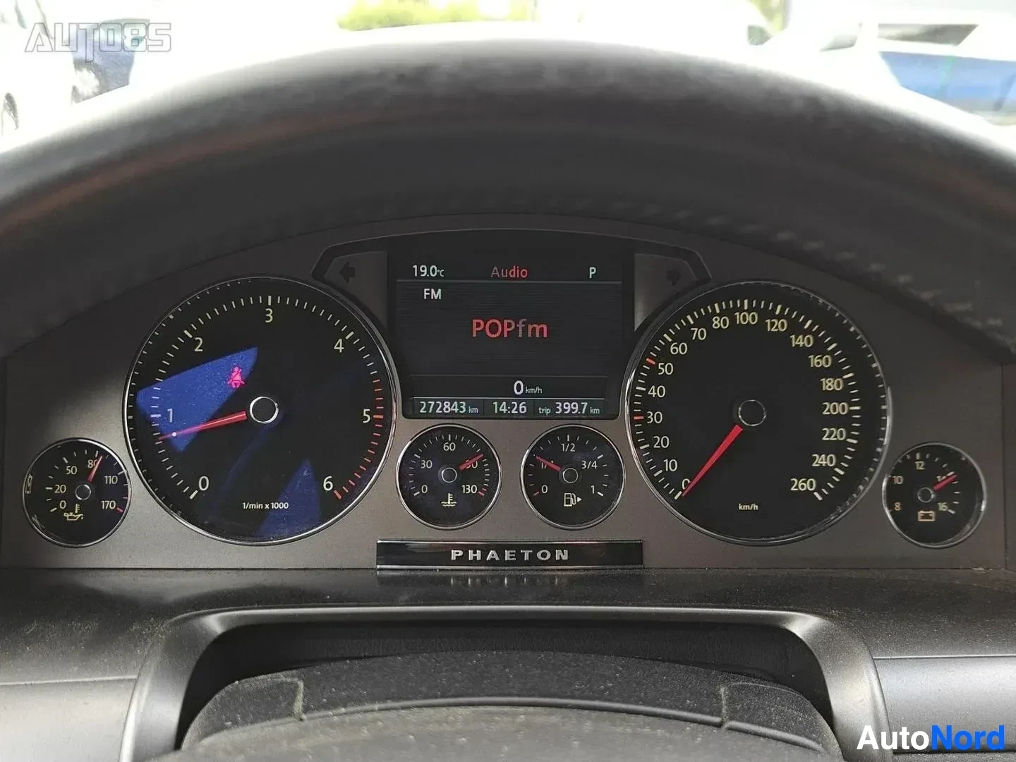 Yksityiskohta: Instrumenttipaneeli, jossa näkyvät nopeusmittari, bensiinimittari ja muut mittarit. Näytöllä lukee "POPfm" ja matkamittari näyttää 272843 km ja 14:26.