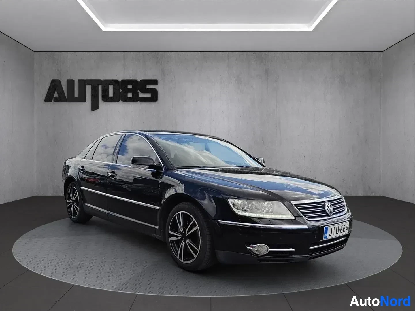 Sivulta: Musta Volkswagen-luksusauto kuvauspaikassa vasemmalle päin, koko ajoneuvo näkyy profiilikuvassa. Rekisterinumero näkyy takimmaisessa osassa. Terävä, hyv