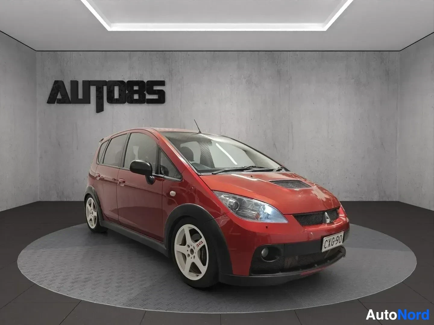 Etuviisto, nokka oikealle: Punainen Mitsubishi Colt viistosta edestä oikealle katsottuna, valkokulmarenkaat, rekisterikilvessä